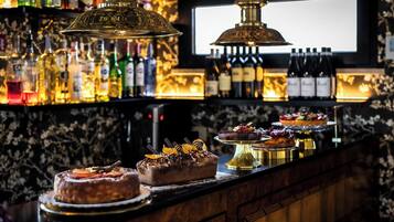 Un espace bar avec un assortiment de bouteilles, un écran de télévision et une variété de desserts présentés.