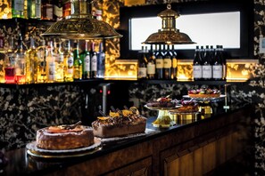 Un espace bar avec un assortiment de bouteilles, un écran de télévision et une variété de desserts présentés.