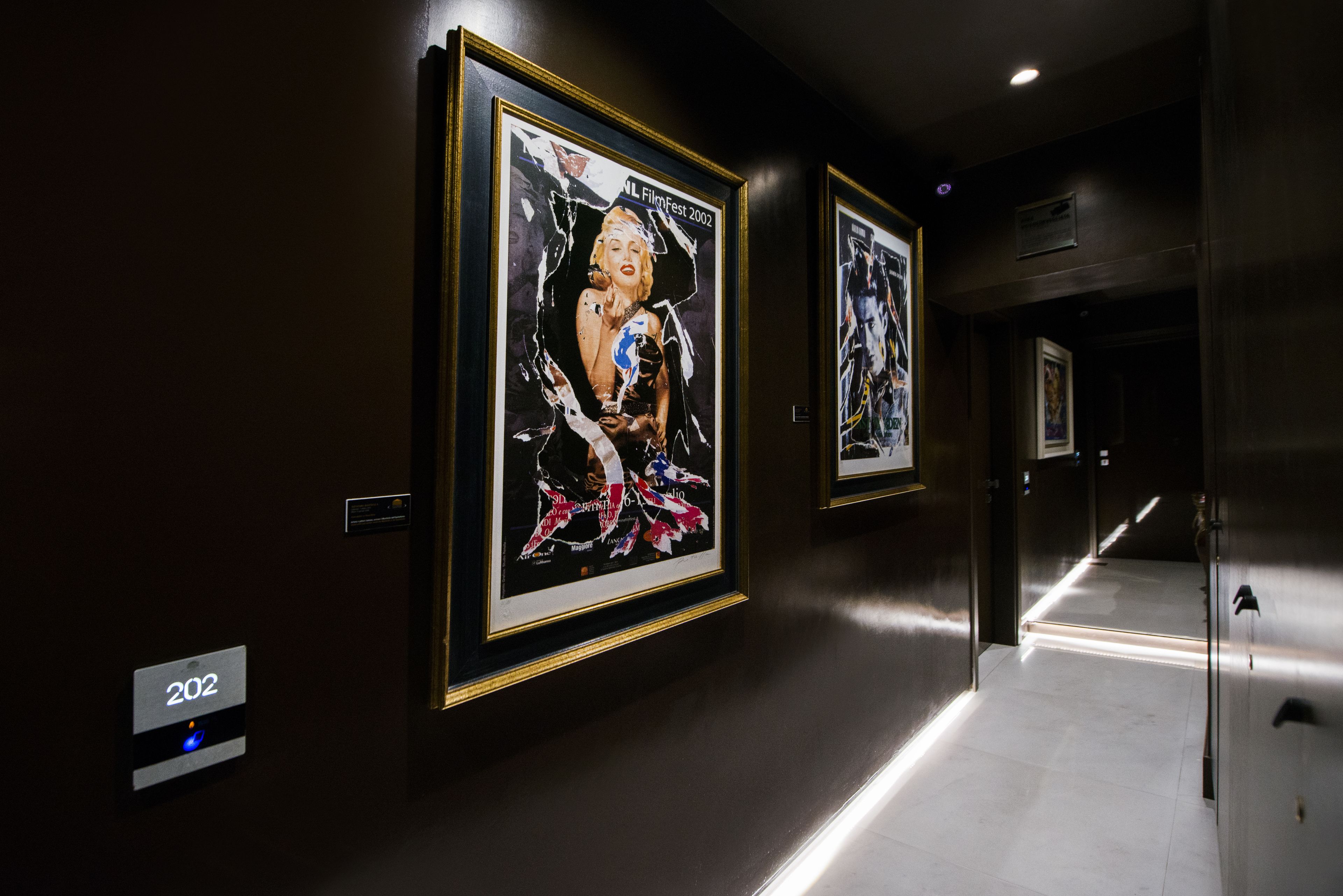 A hallway with framed artwork on the walls, a floor number sign, and a door with a handle.