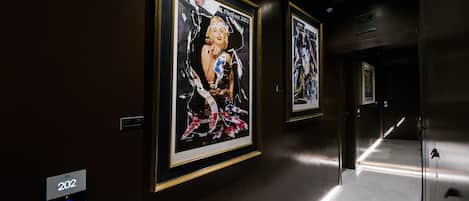 A hallway with framed artwork on the walls, a floor number sign, and a door with a handle.