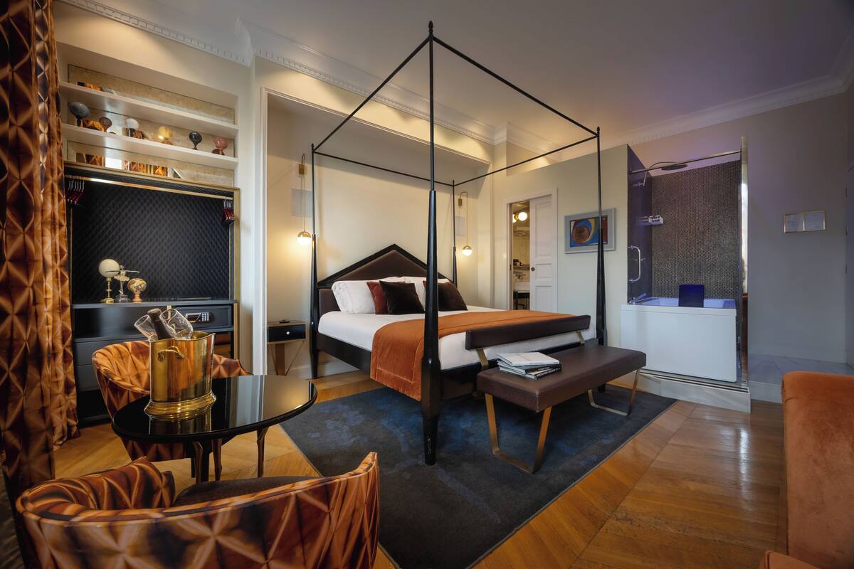 A modern bedroom with a four-poster bed, a desk with a chair, and a walk-in closet.
