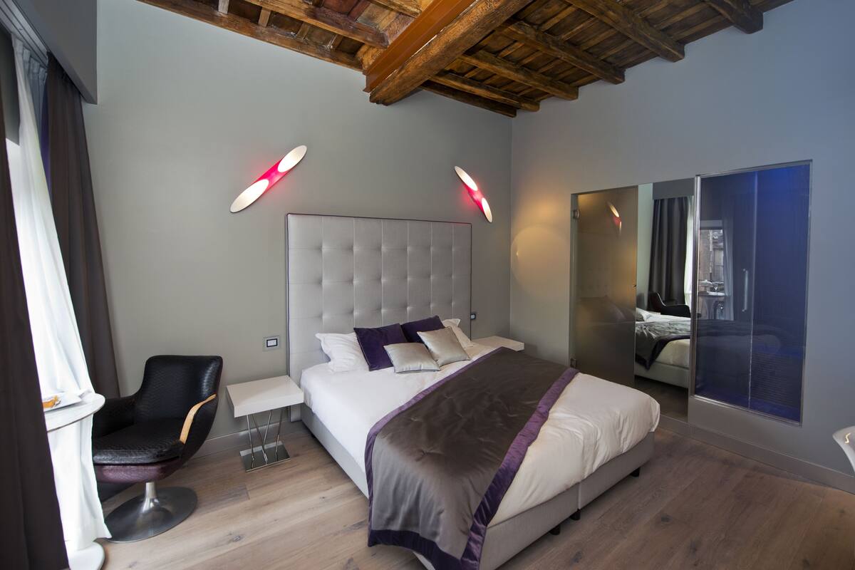 A modern bedroom with a large bed, a chair, a bedside table, and a mirror.