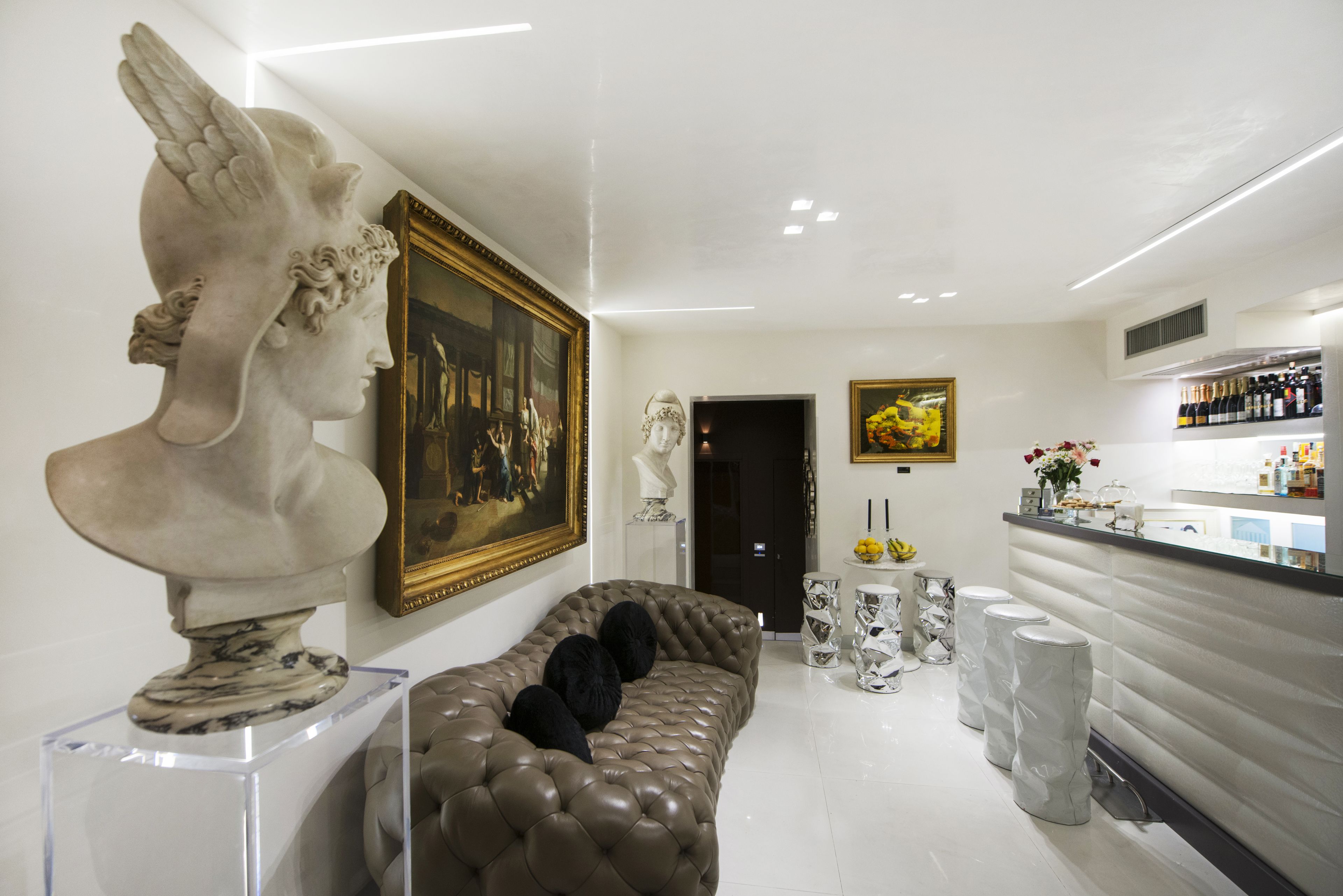 A modern interior with a tufted leather sofa, a bust sculpture, and a bar area with bottles.