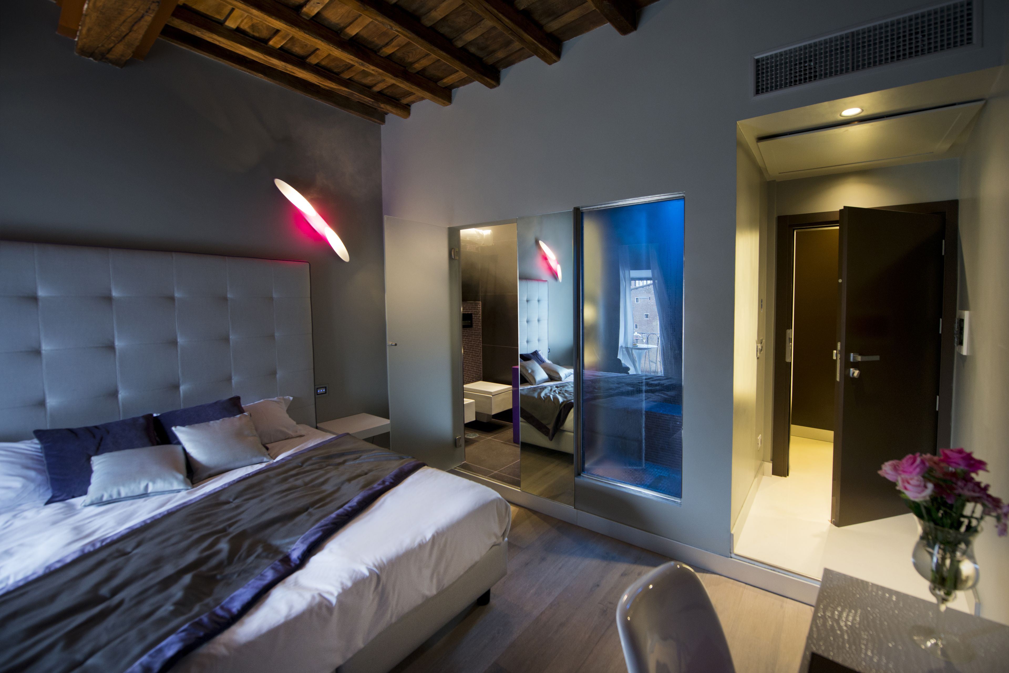 Une chambre d’hôtel moderne, dotée d’un grand lit, d’un bureau et d’une salle de bain visible à travers une paroi en verre.