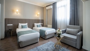 A hotel room with two single beds, a sofa, a small table with a vase, and a large window with curtains.
