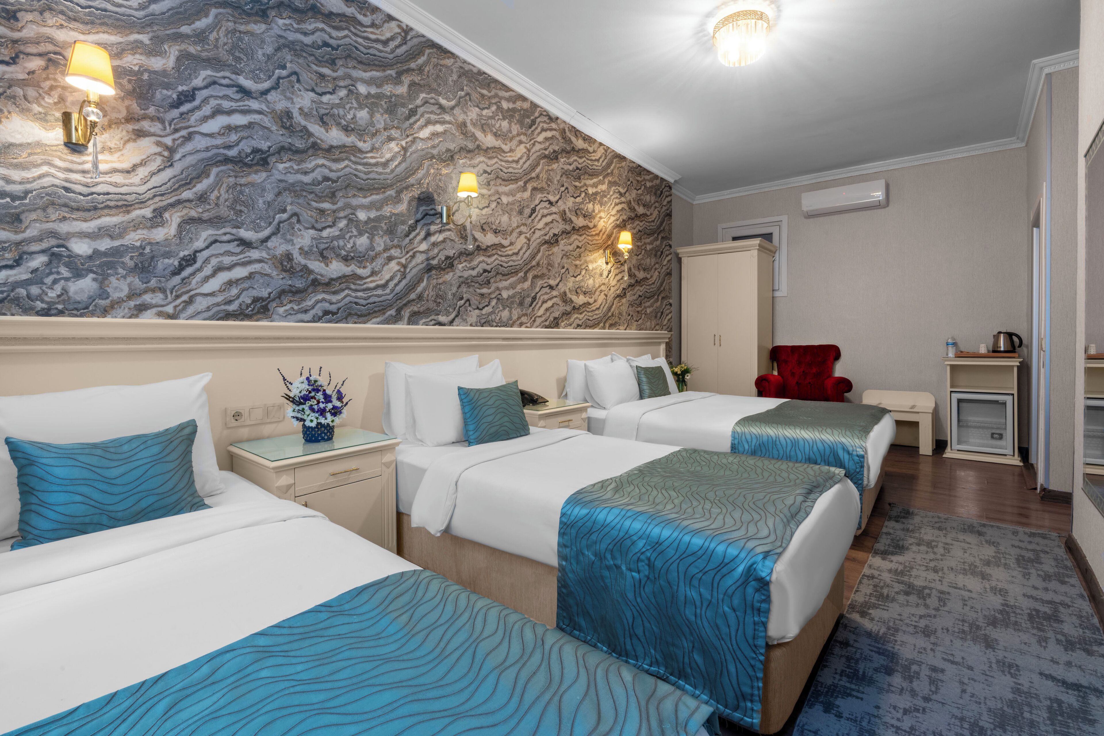 A hotel room with three beds, marble-patterned walls, and a red chair.