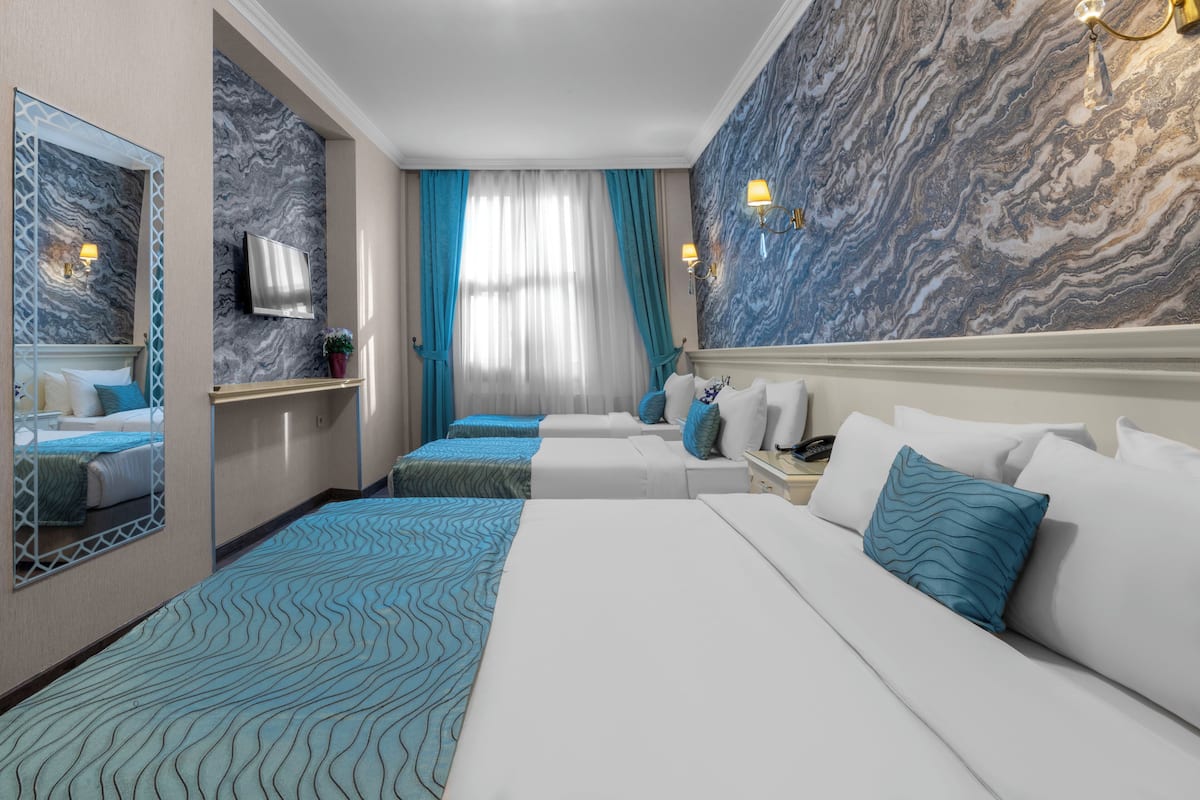 A hotel room with a large bed, two smaller beds, a TV, and a marble wall.