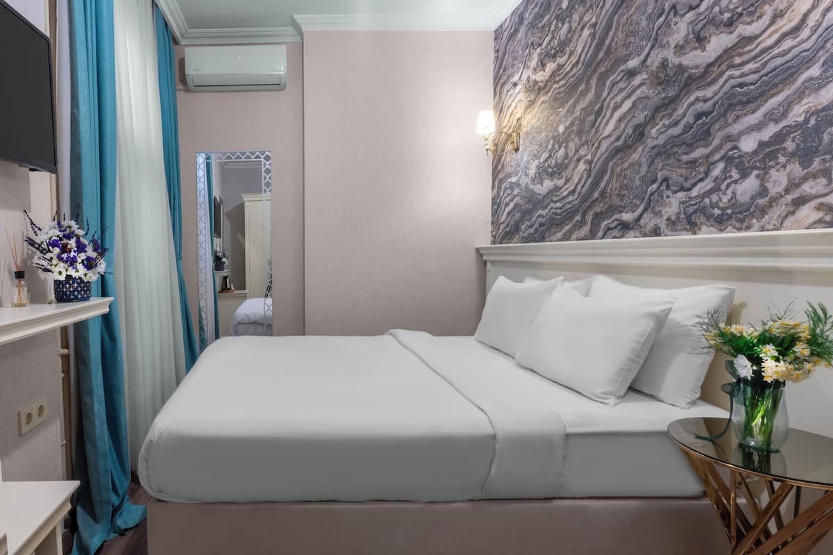 A neatly made bed with white linens, a vase with flowers on a side table, and a marble-patterned wall.