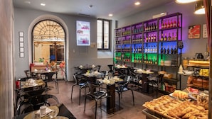 Interior de un restaurante con mesas y sillas, una estantería de vinos y una vitrina con postres.