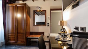 Una habitación de hotel con un armario de madera, una cama con cabecero, una mesita de noche con lámpara y una cafetera.