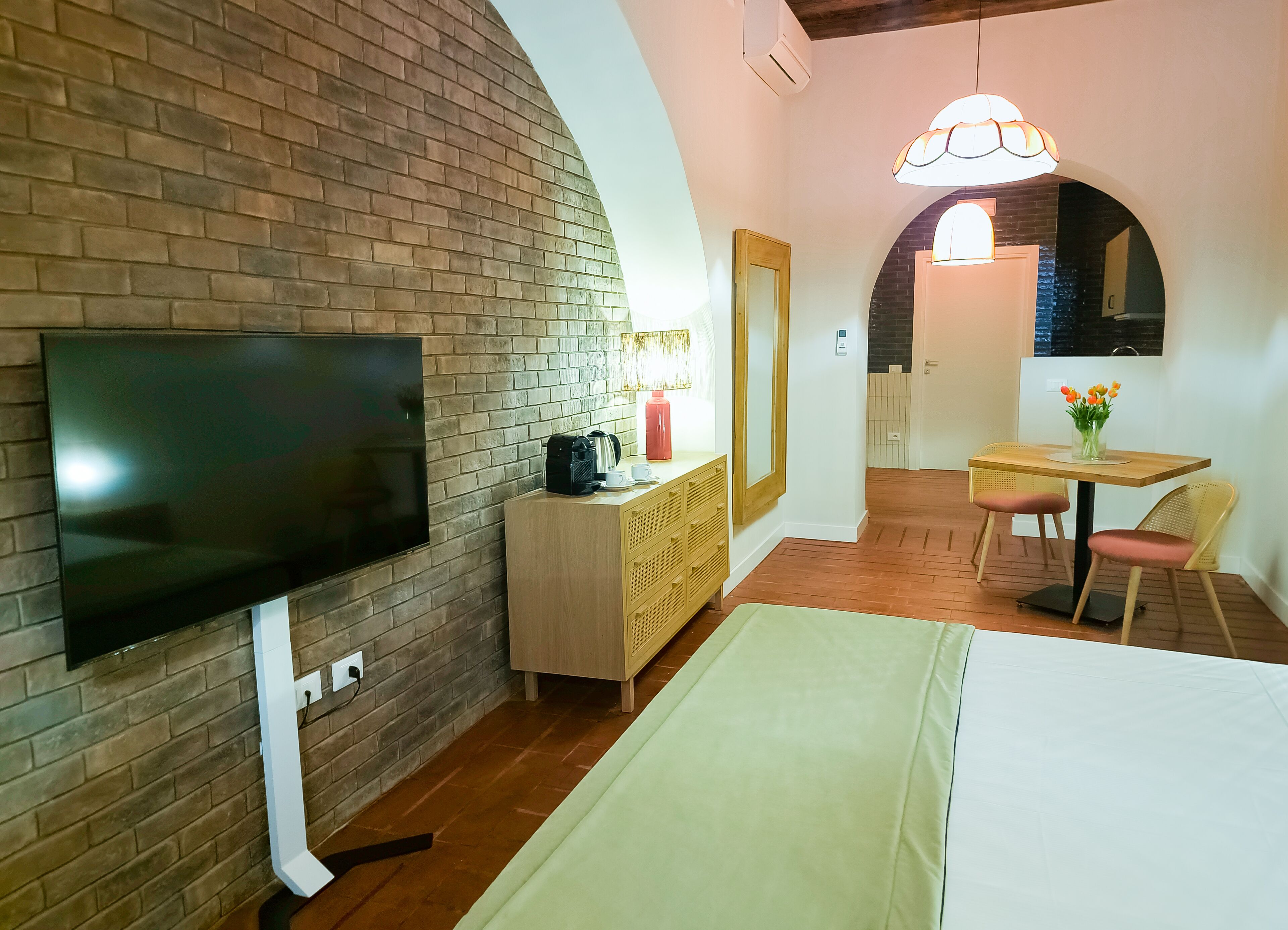 Une chambre d’hôtel avec un mur en briques, un téléviseur à écran plat, une commode en bois, un bureau avec une chaise et un grand miroir.