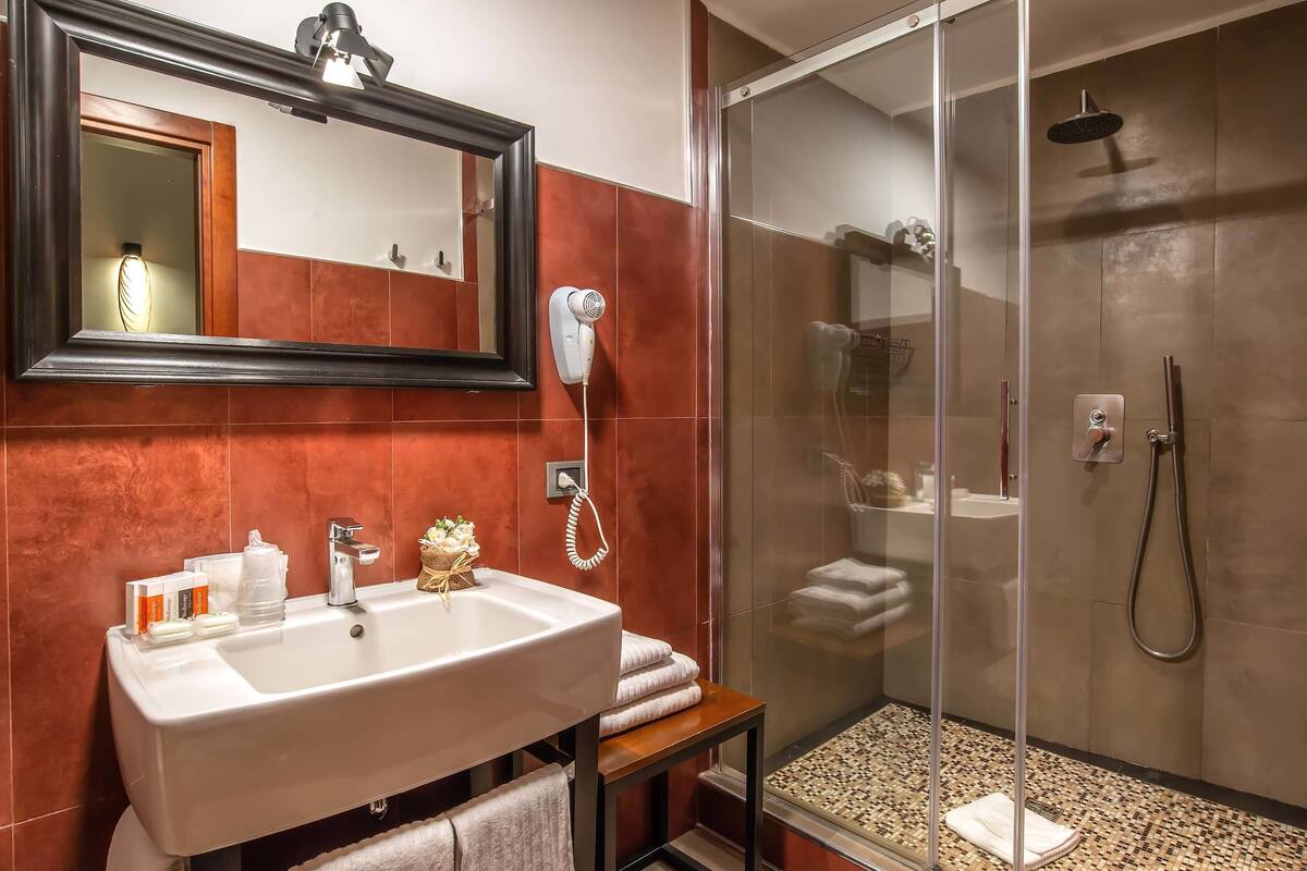 A bathroom with a large mirror, a sink, a hairdryer, and a glass-enclosed shower.