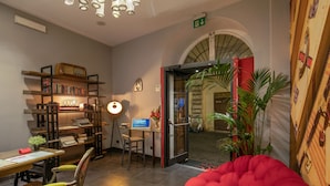 Una habitación acogedora con un sillón de peluche rojo, un escritorio con ordenador, una estantería y una puerta que da a un balcón.