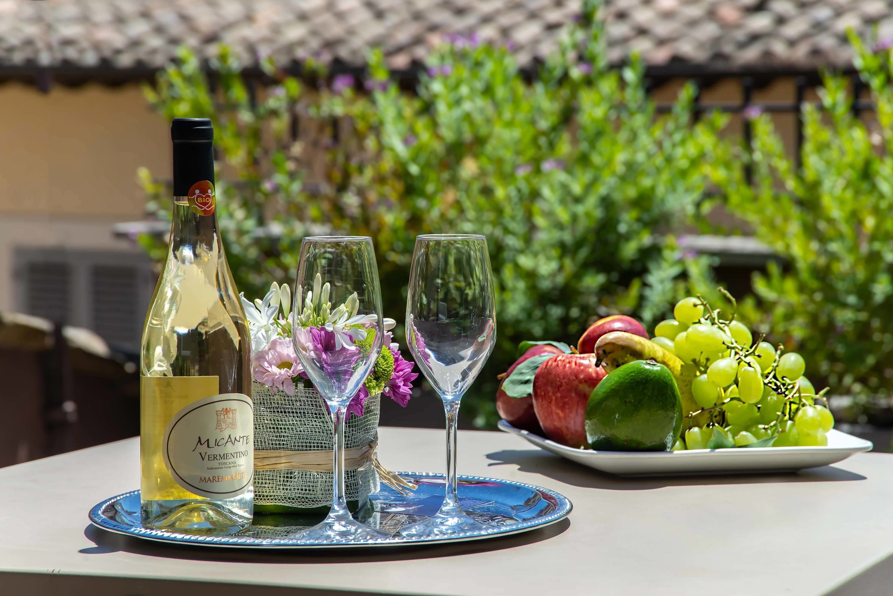 Uma garrafa de vinho, duas taças e um prato com frutas sobre uma mesa ao ar livre.