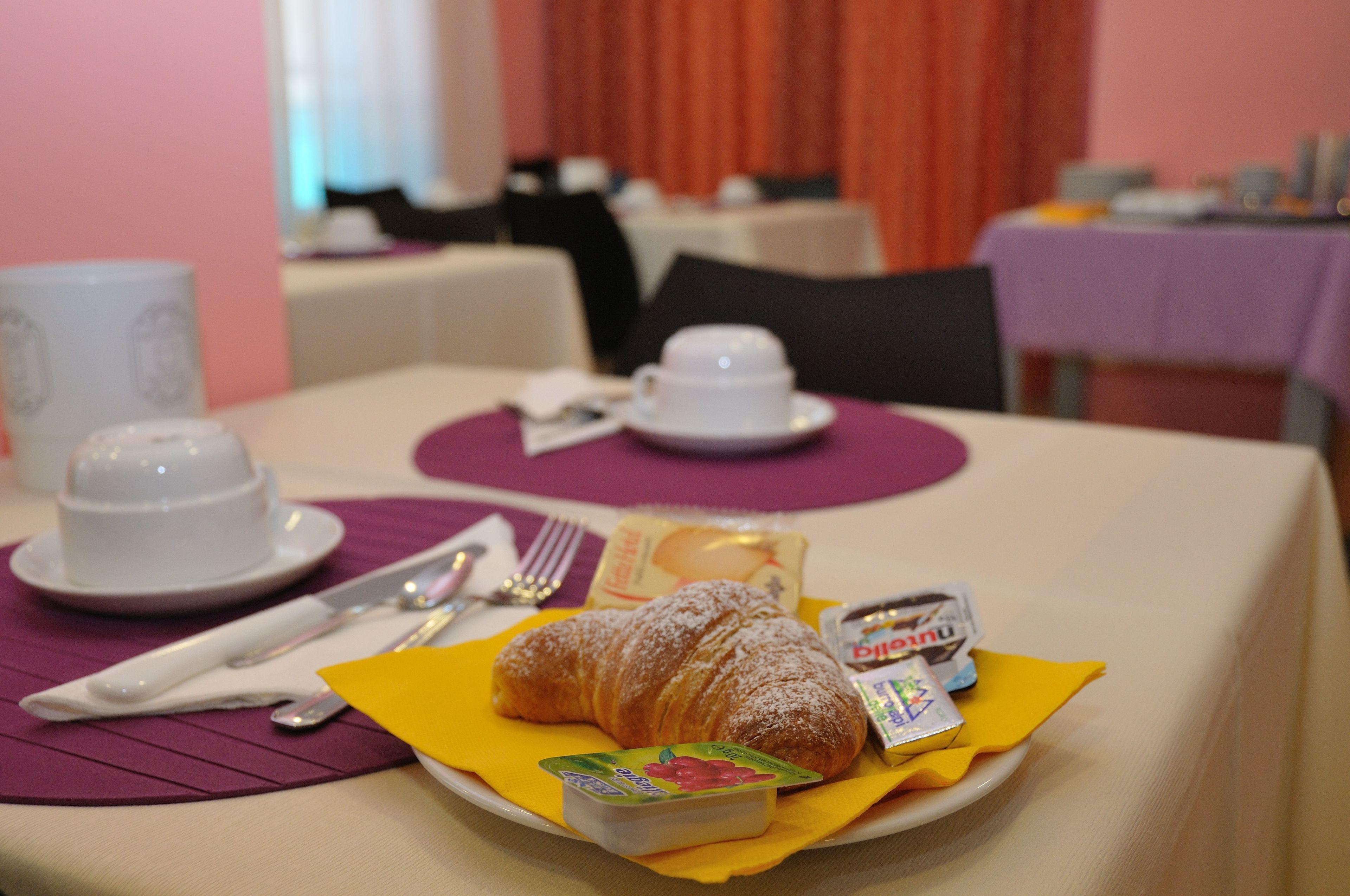 A breakfast setting with a croissant, yogurt, and a beverage on a table.