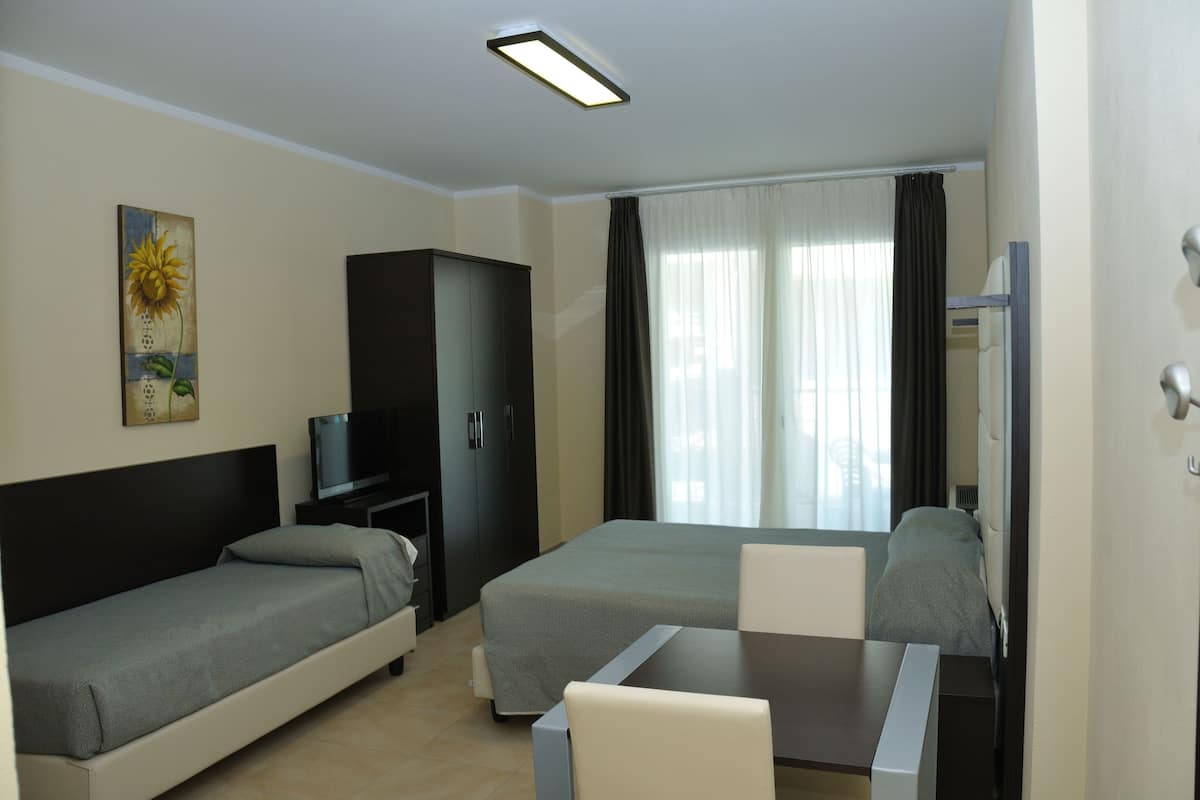 A hotel room with a bed, a desk, a chair, a TV, a wardrobe, and a painting.