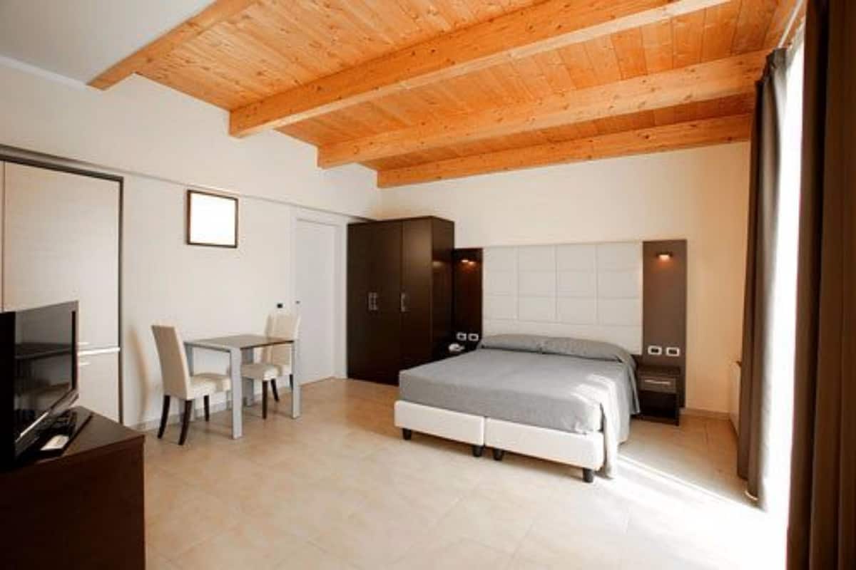 A bedroom with a bed, a desk, a chair, and a TV.