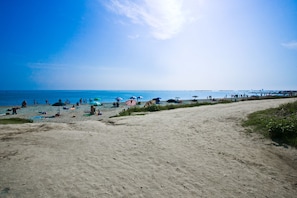 Una playa con gente tomando el sol y nadando, sombrillas y un cielo despejado.
