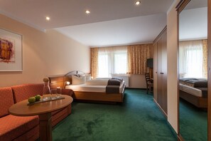 A hotel room with a bed, a sofa, a table with apples and glasses, a TV, and a window with curtains.
