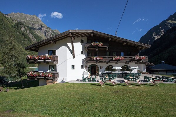 A chalet with a balcony, outdoor seating, and a mountain backdrop.