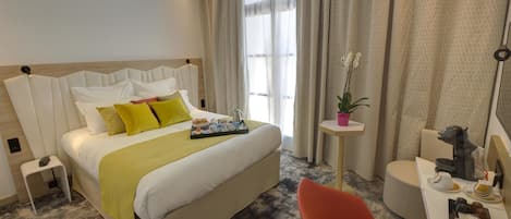 A hotel room with a bed, bedside table, chair, and a small desk with a coffee machine.