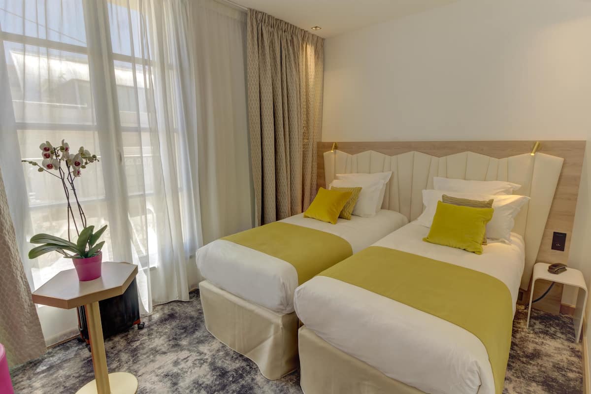 A hotel room with two beds, a small table with a potted plant, and a nightstand with a phone.