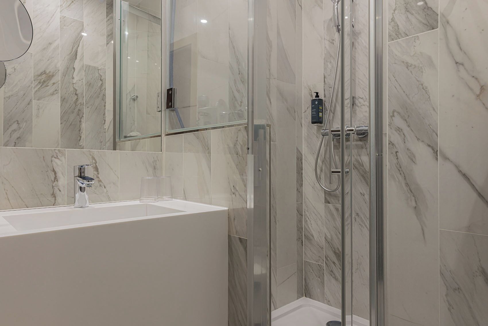 A modern bathroom with a glass-enclosed shower, a white sink, and marble walls.