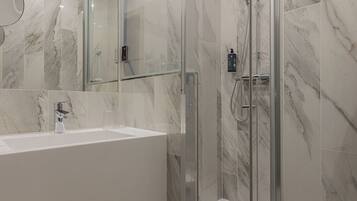 A modern bathroom with a glass-enclosed shower, a white sink, and marble walls.