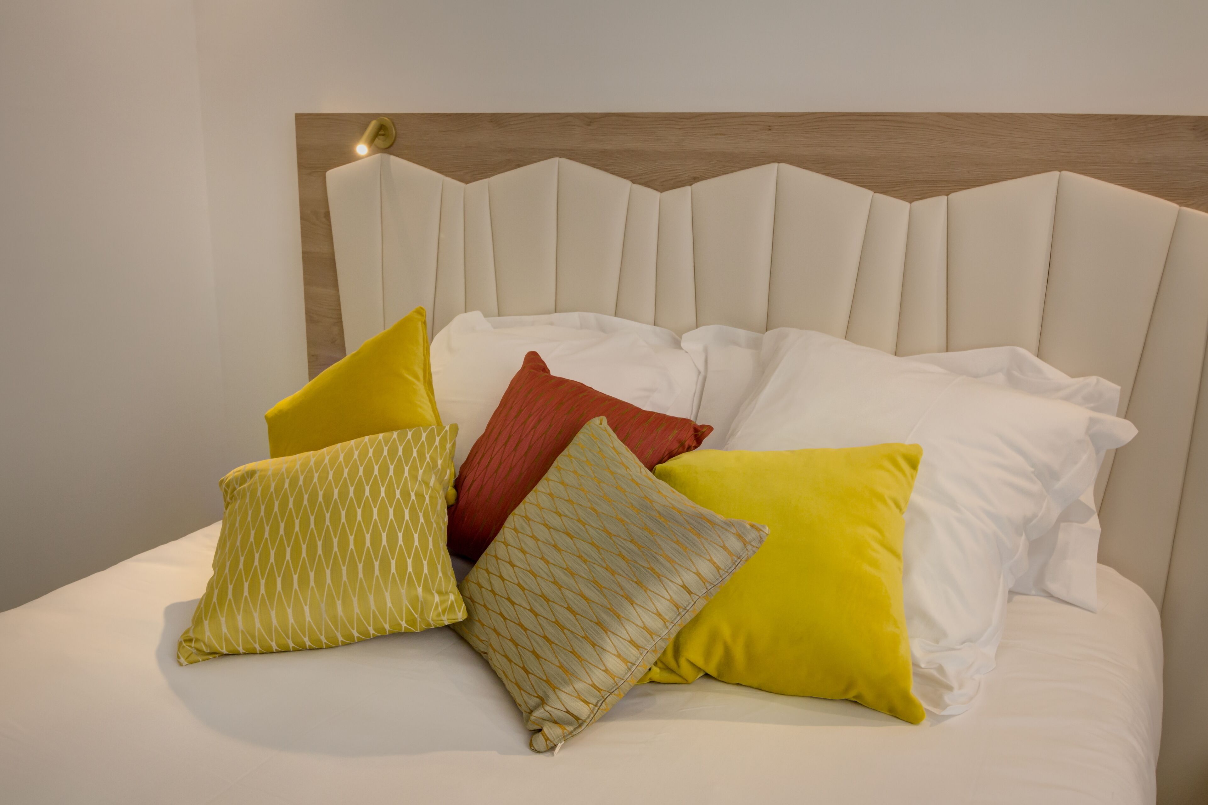 A bed with a headboard, multiple pillows, and a wall-mounted light fixture.