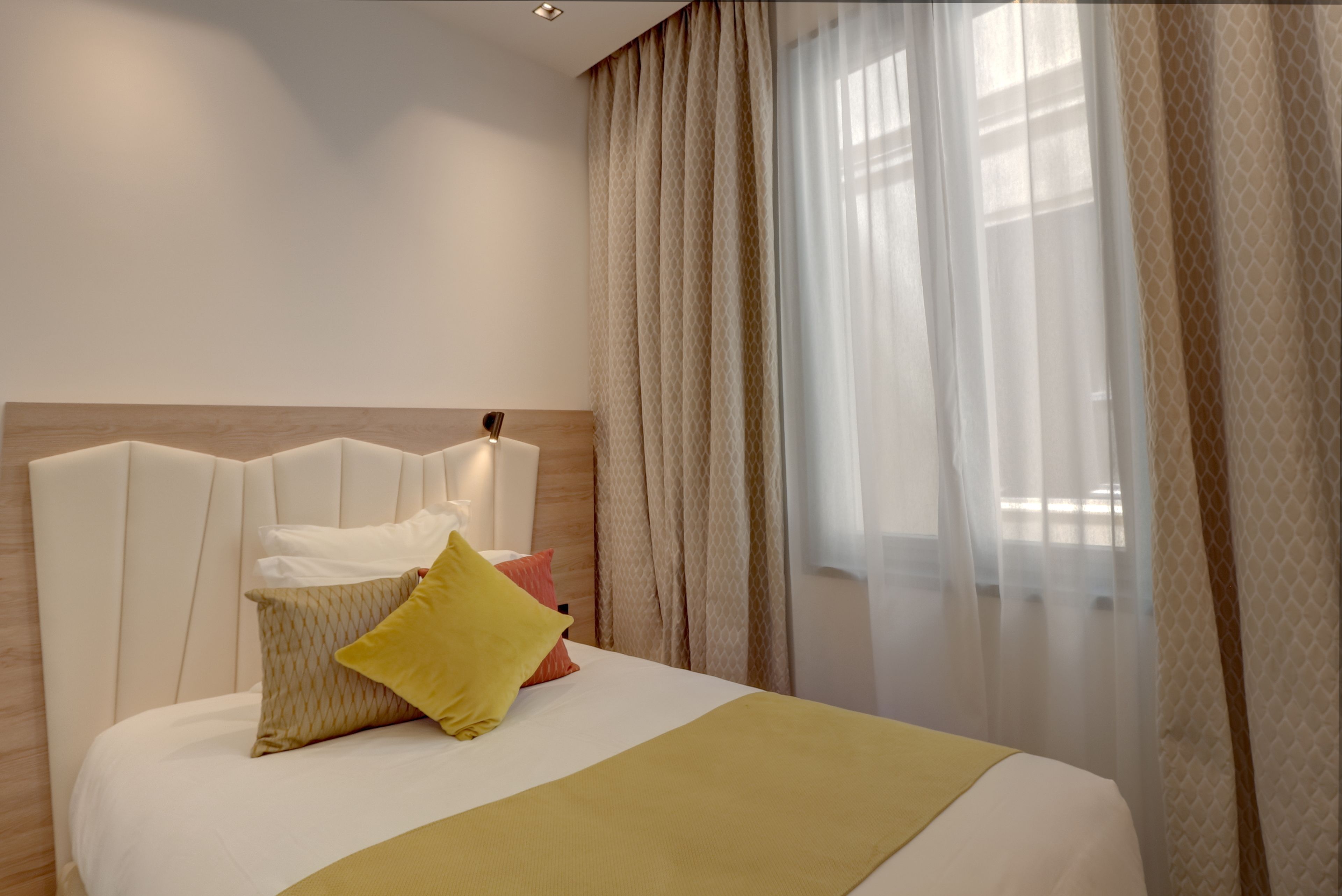 Ein Hotelzimmer mit einem großen Bett, einem Kopfteil und durchsichtigen Vorhängen.