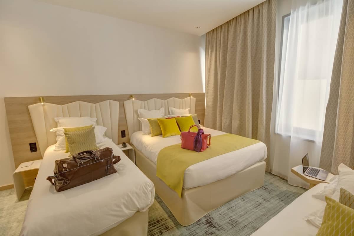 A hotel room with two beds, a laptop on a side table, and a suitcase on the floor.