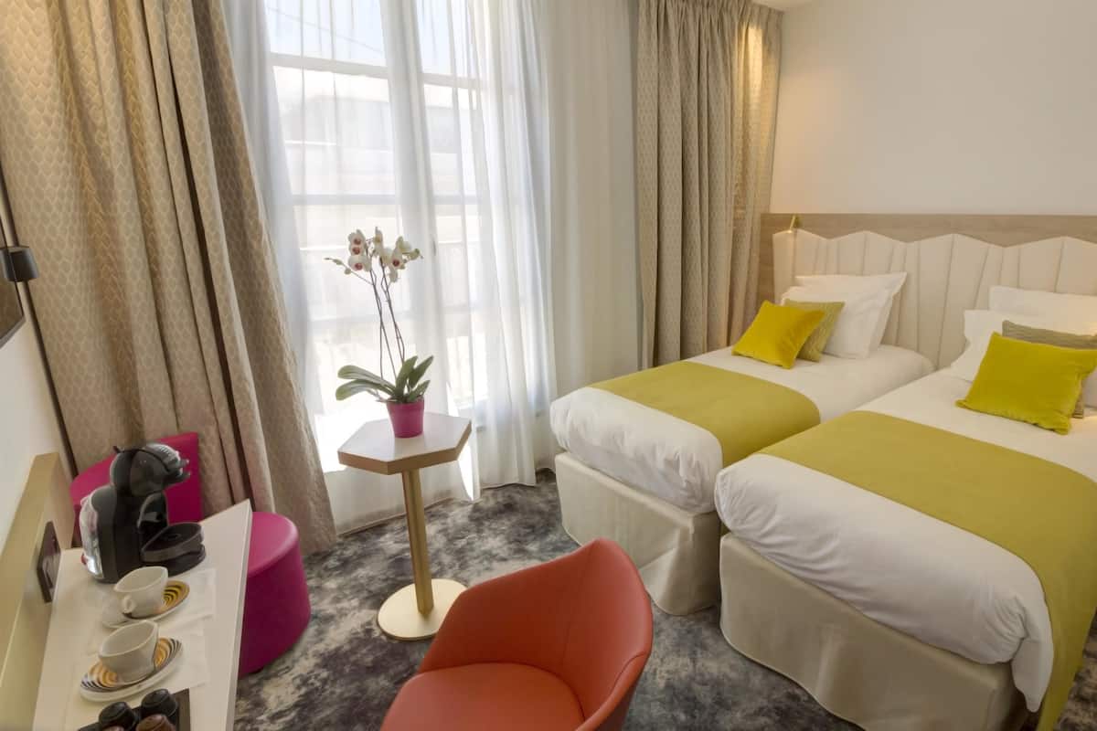 A hotel room with two beds, a small table with a potted plant, a coffee machine, and a chair.