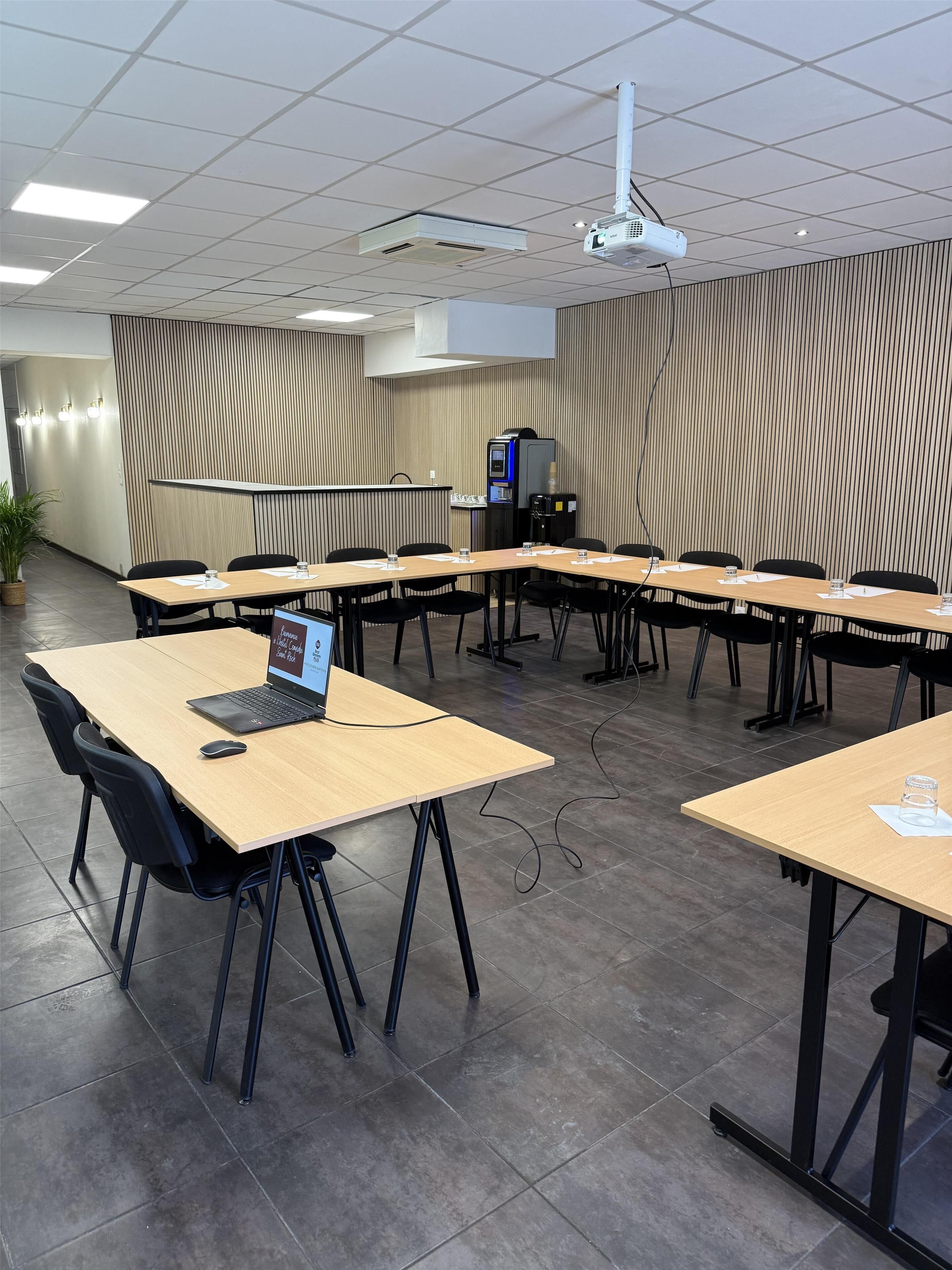 Een vergaderruimte met een lange tafel, stoelen, een laptop en een beamer.