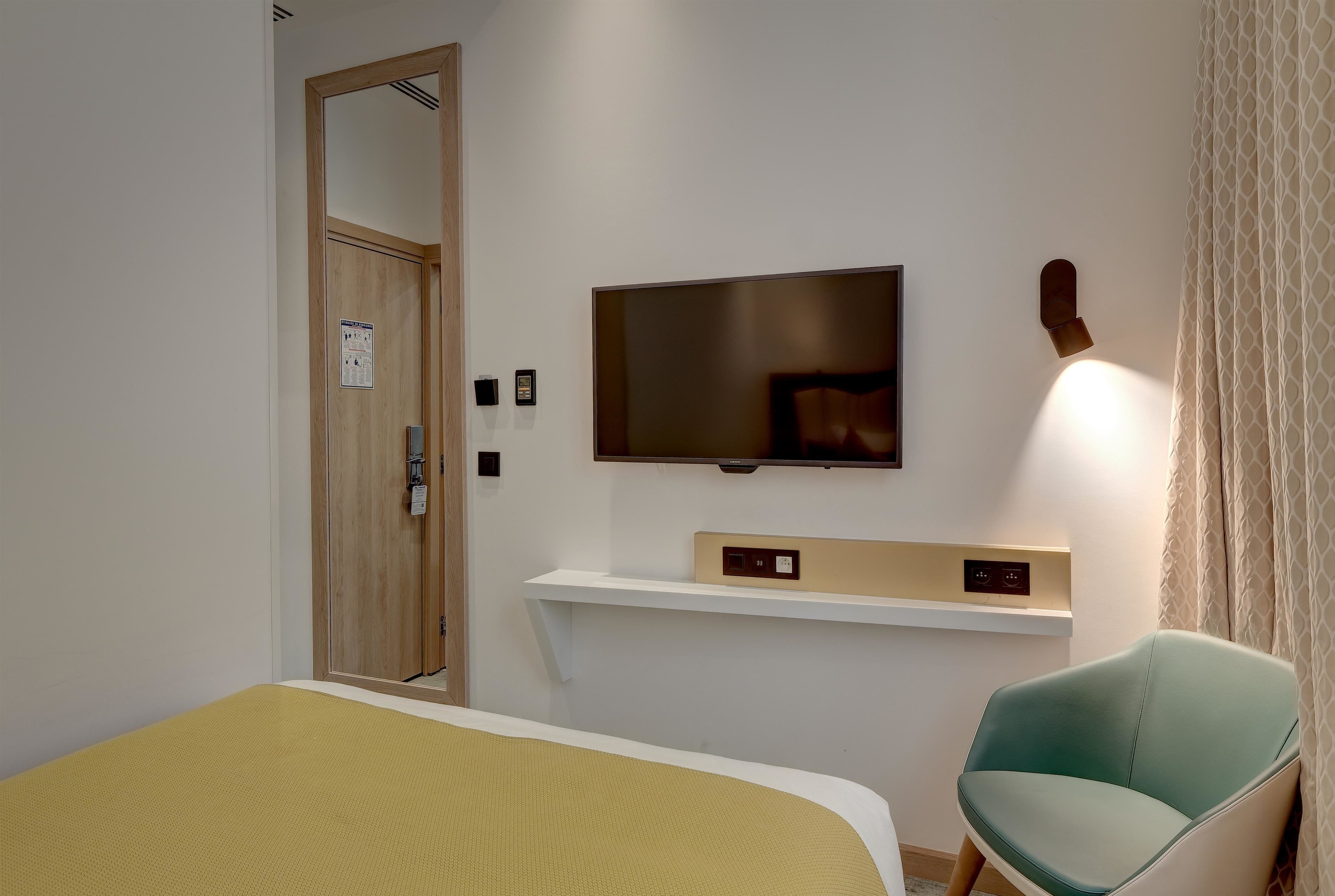 Une chambre d’hôtel avec un lit, un téléviseur fixé au mur, une petite étagère et une chaise.