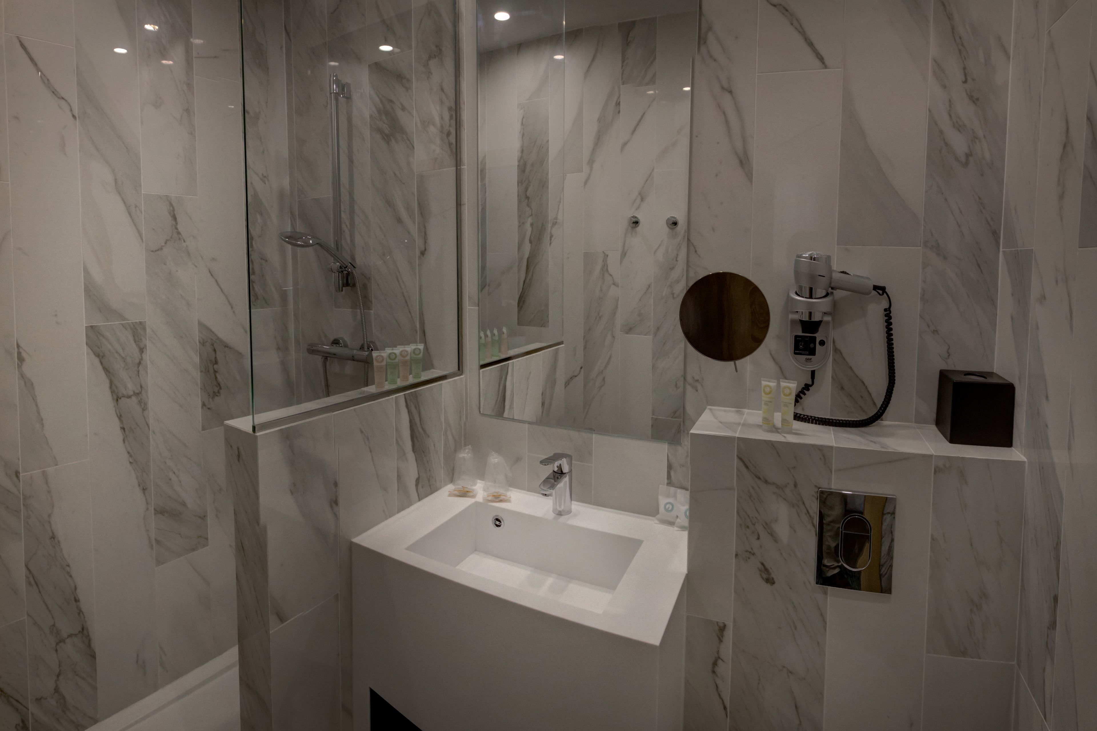 A modern bathroom with a marble-tiled shower, a white sink, and a mirror.