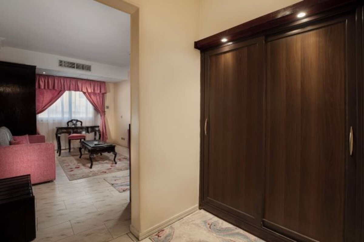 Una habitación con un amplio armario de madera, un sofá rosa, una mesita y una silla.