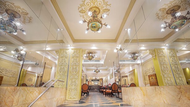 Un vaste hall d’hôtel, avec un sol en marbre, des colonnes richement décorées et de magnifiques lustres.