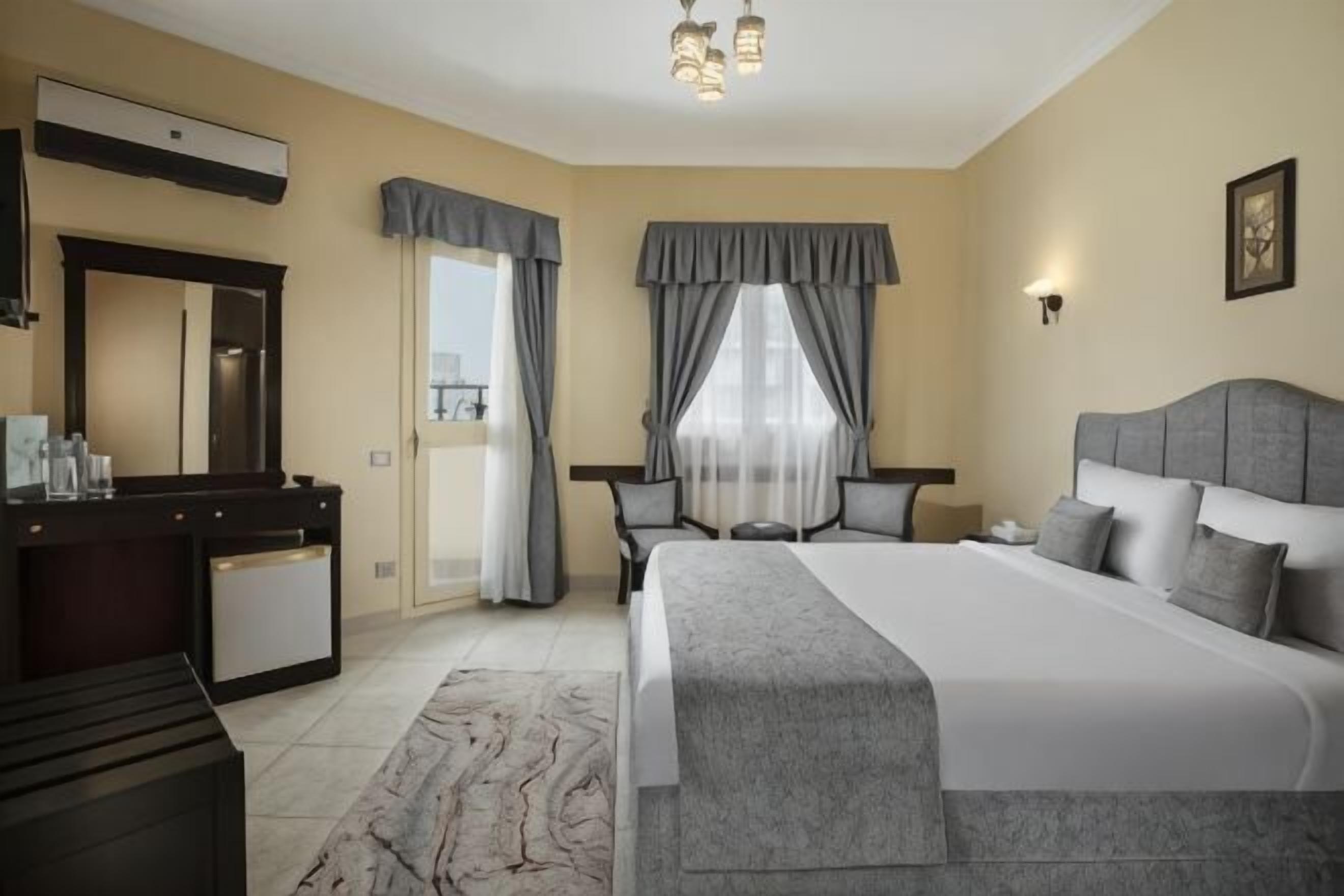 Ein Hotelzimmer mit einem großen Bett, einem Schreibtisch, einem Sessel, einem Schminktisch und einem Fenster mit Vorhängen.