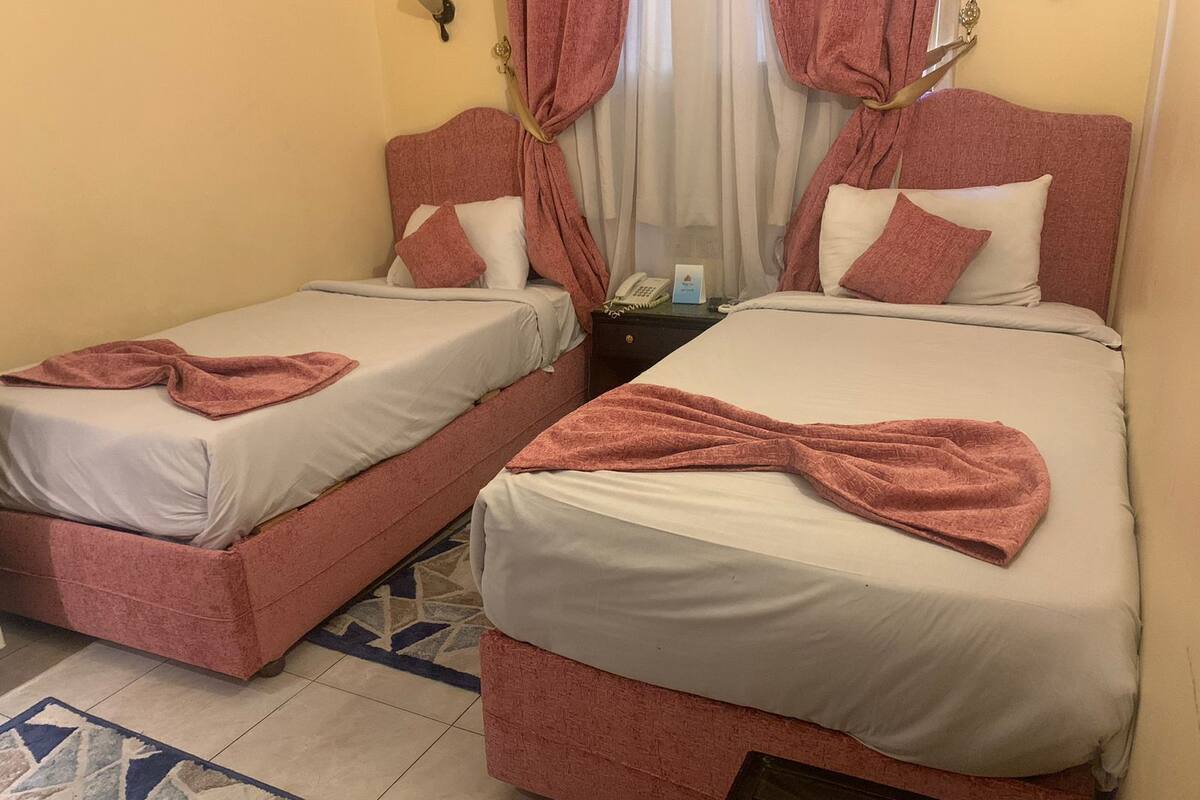Quarto de hotel com duas camas, cada uma com toalha rosa e roupa de cama branca.