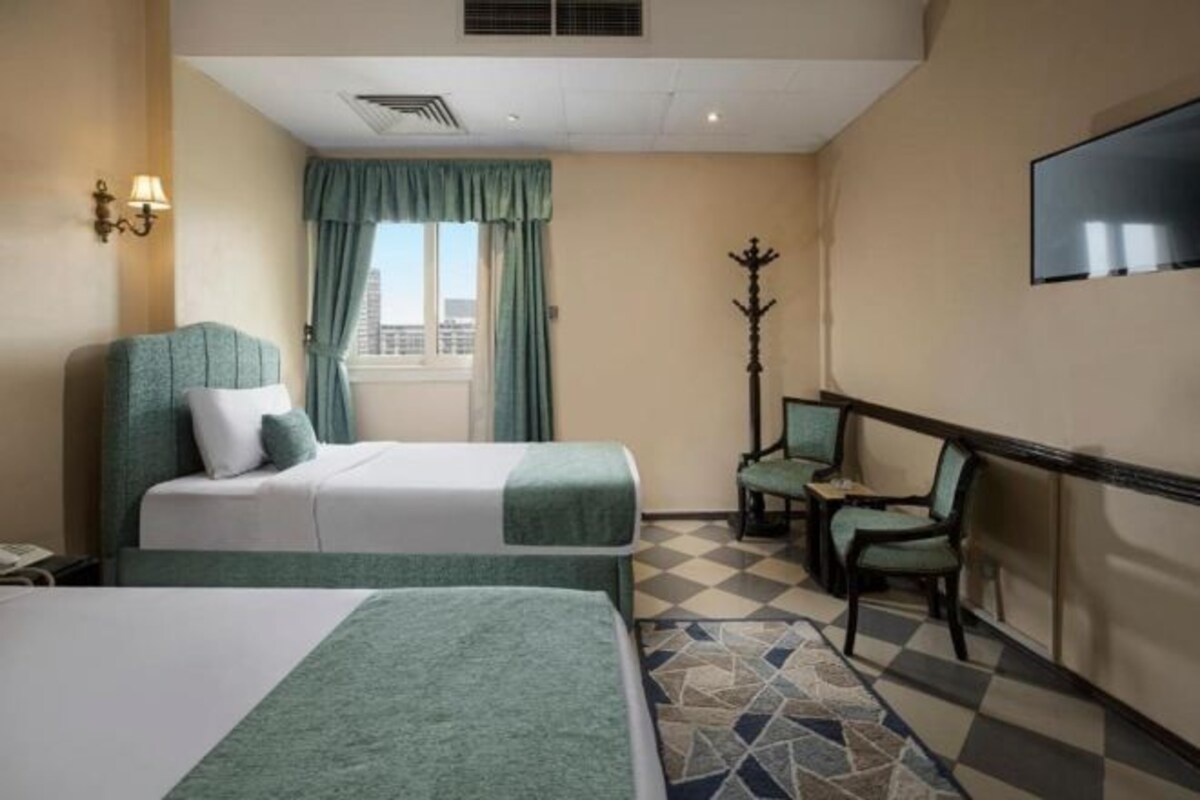 Habitación de hotel con dos camas, un televisor, perchero y piso a cuadros.