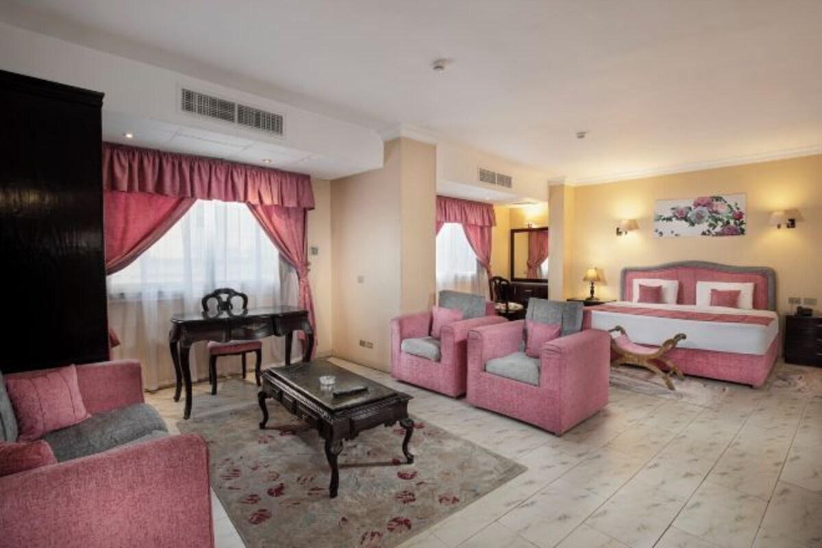 A hotel room with a sofa set, a dining table, a coffee table, a bed with a headboard, and a painting on the wall.
