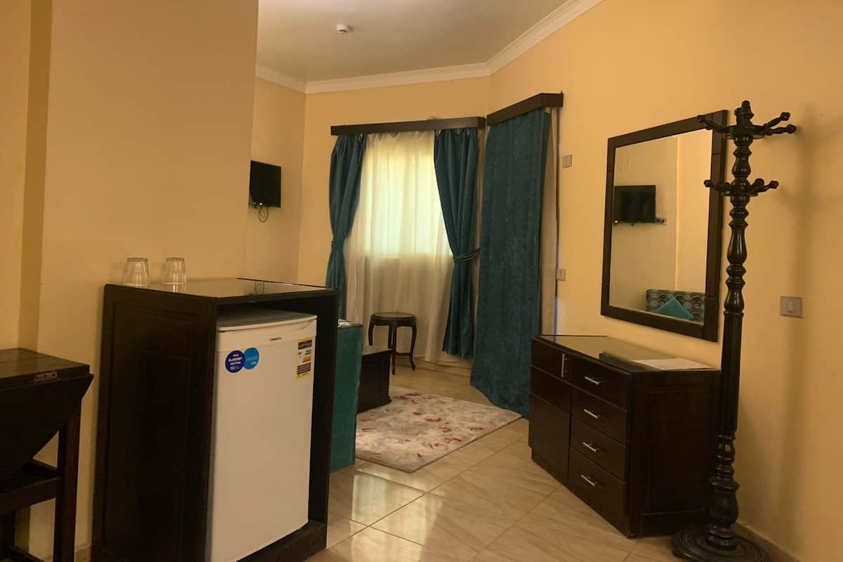 Quarto de hotel compacto com cozinha compacta, um espelho, um banquinho pequeno e uma janela com cortinas.