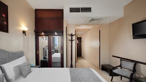 Une chambre d’hôtel avec un grand lit, une chaise, un téléviseur et un porte-manteau.