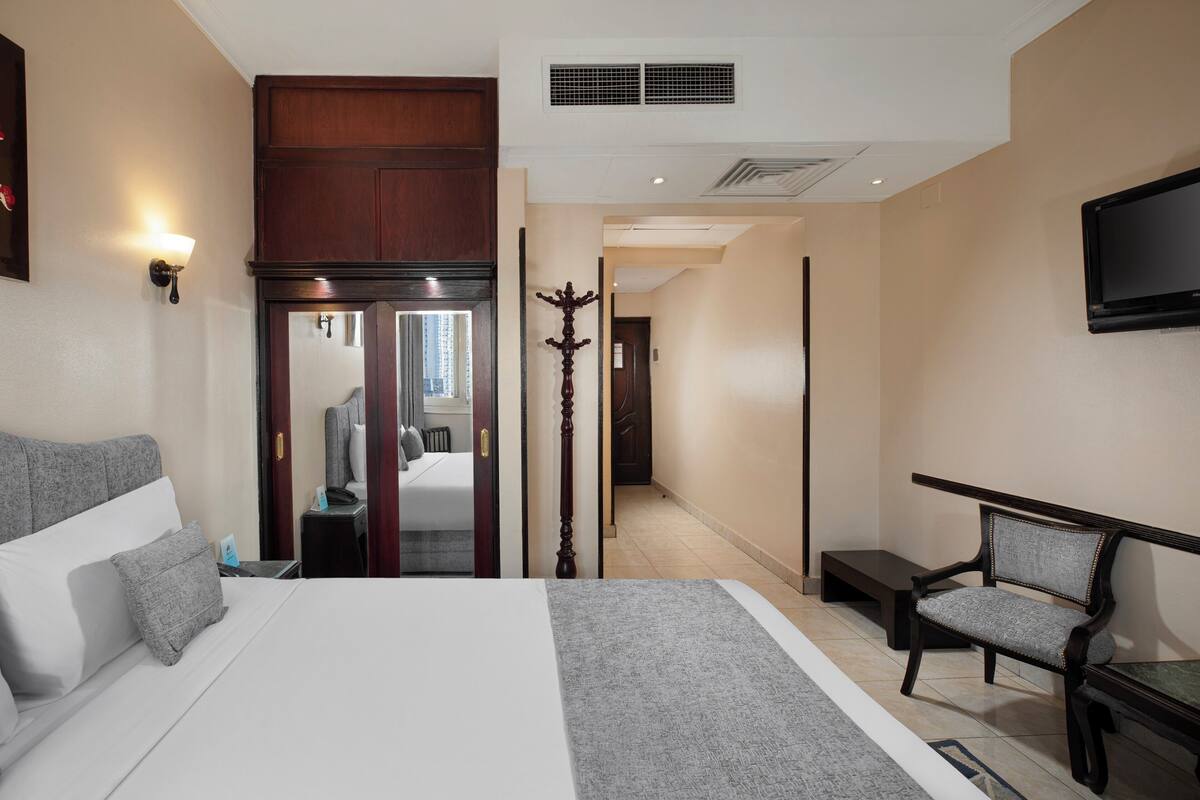 Quarto de hotel com uma cama grande, uma cadeira, uma TV e um cabideiro.