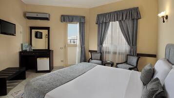 A hotel room with a large bed, a desk with a mirror, a chair, a small table, and a TV.