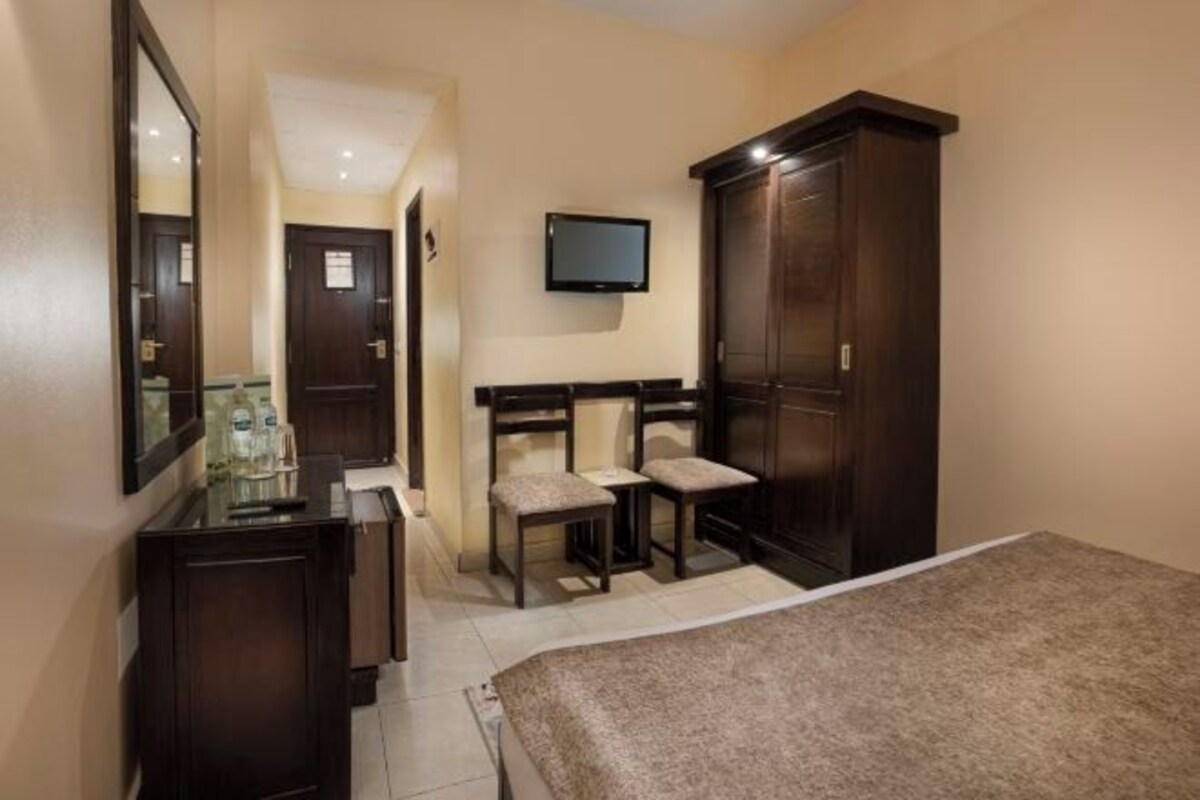 A bedroom with a bed, a dresser, a TV mounted on the wall, and two chairs.