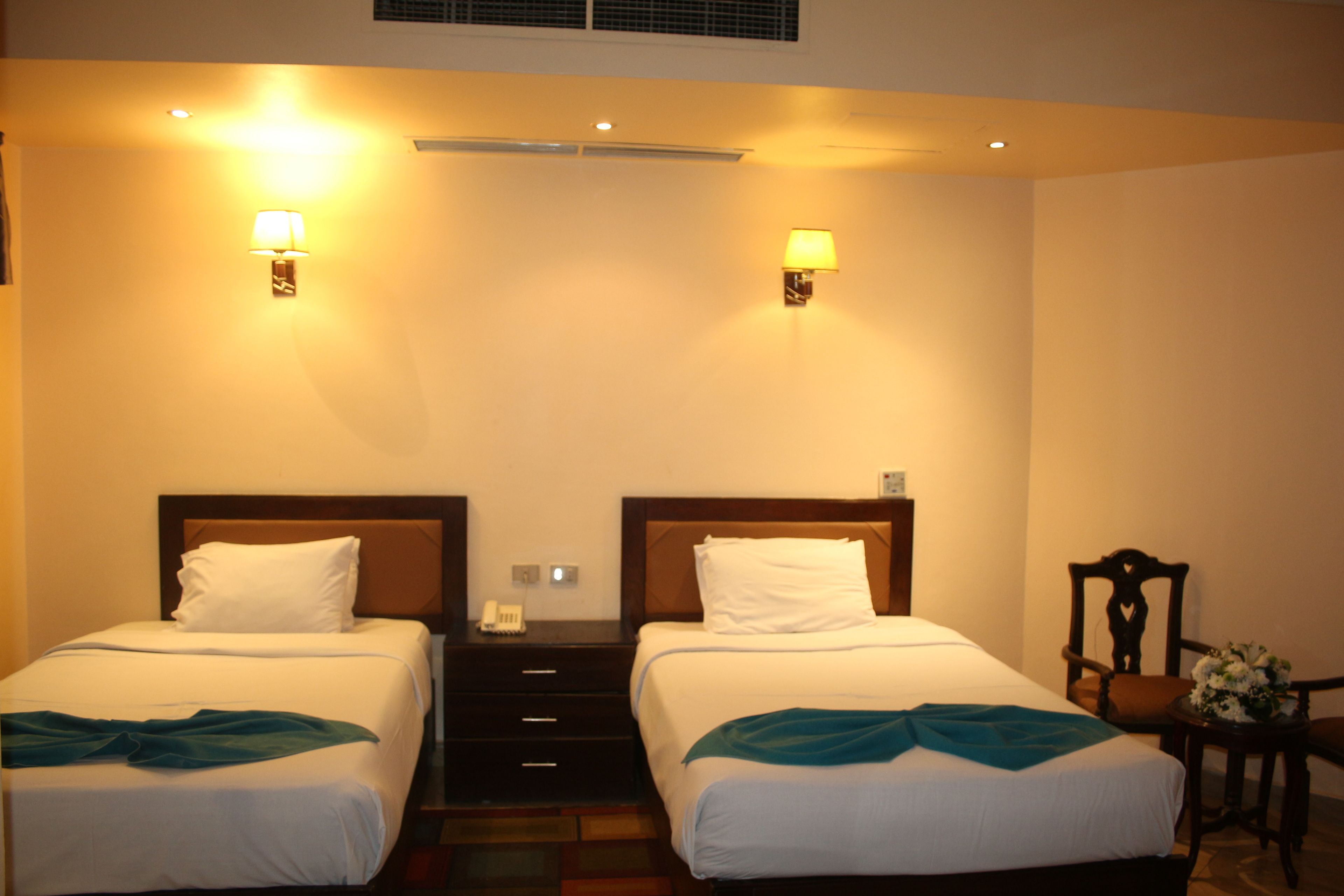 A hotel room with two beds, a desk, a chair, and a small table with a vase.