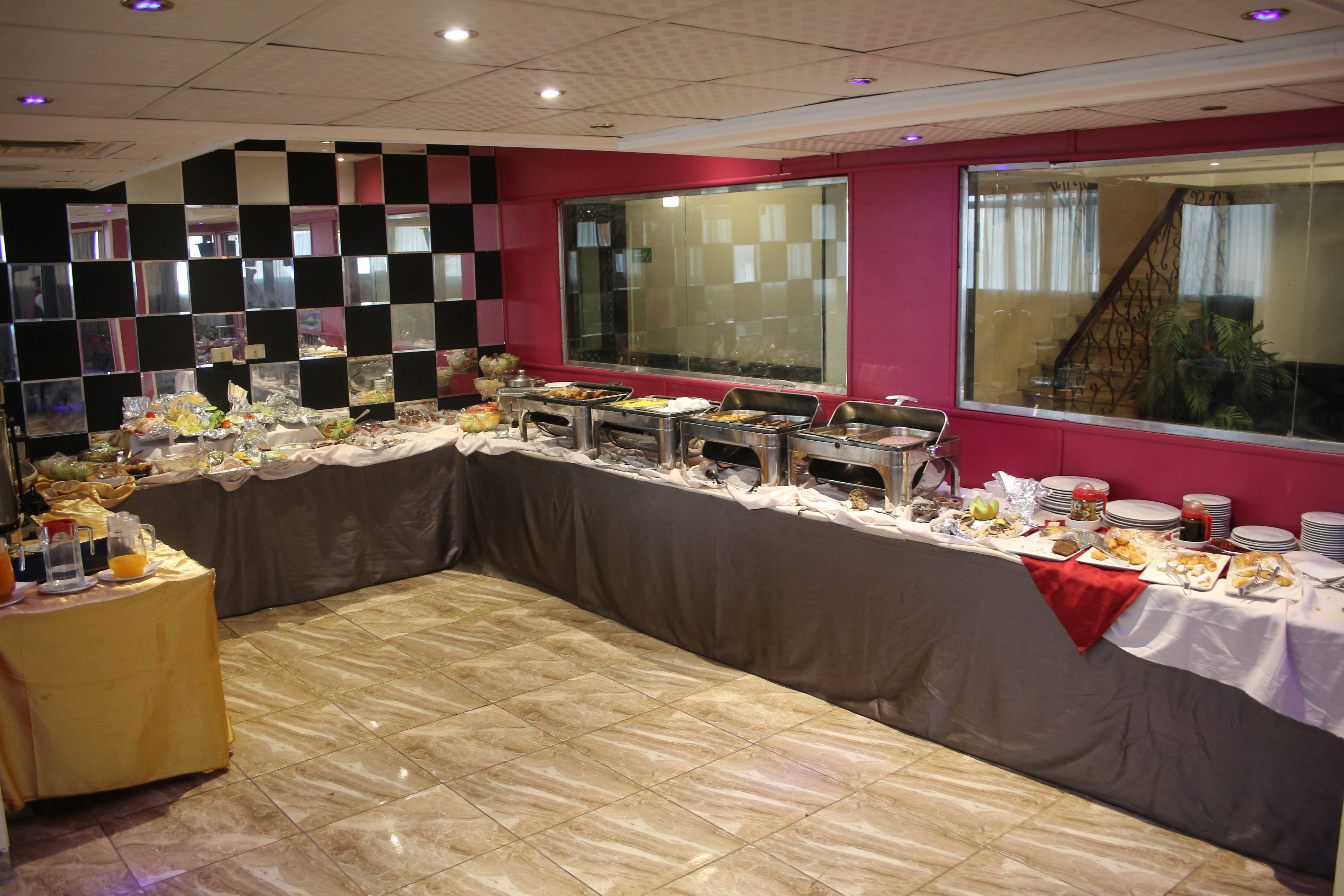 A buffet setup with various food items and drinks, a tiled floor, and a checkered wall pattern.