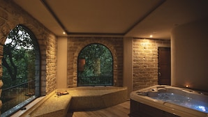 Un cuarto de spa con pared de piedra, ventana con vista a árboles, jacuzzi y una zona de estar.