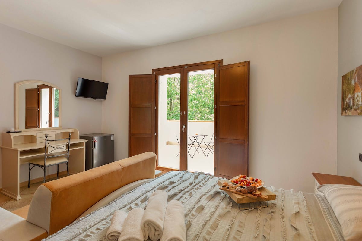 Un dormitorio con cama, escritorio, silla, televisor y un balcón con mesa y sillas.